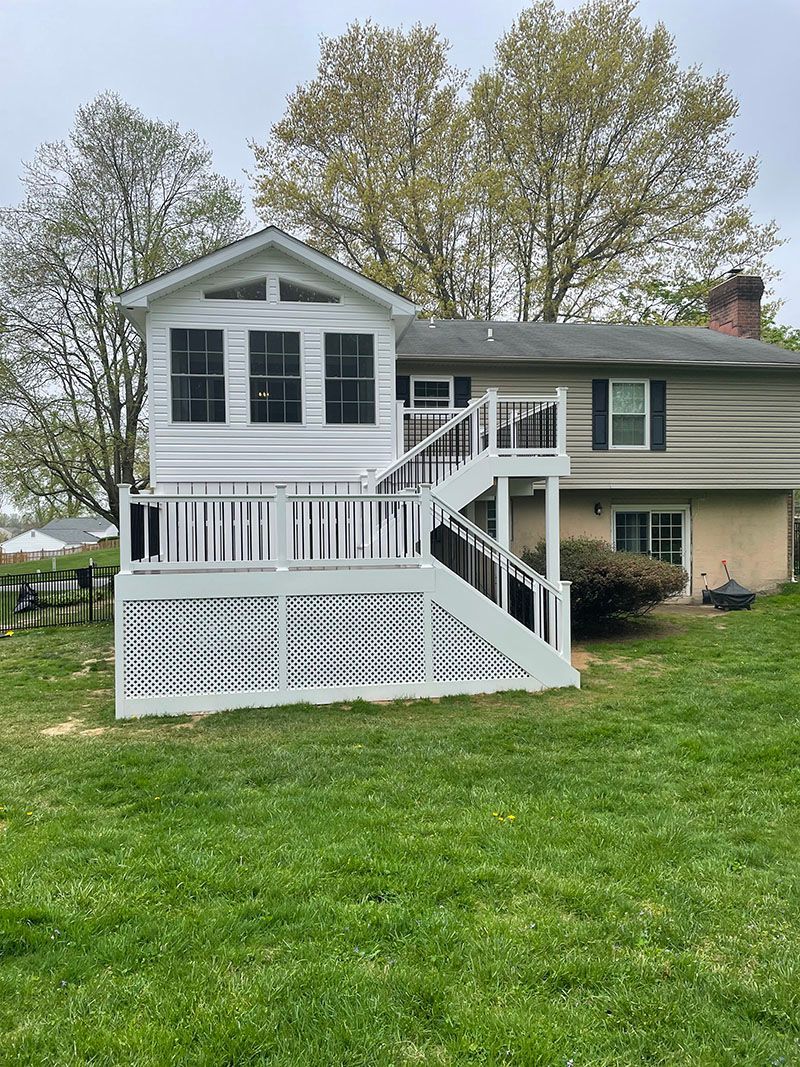 Back of house with large white deck and attached sunroom, set in a grassy yard.
