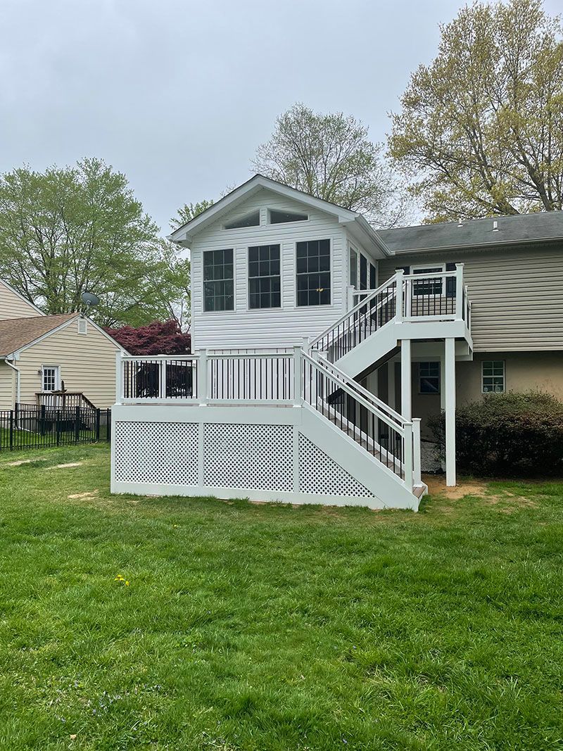 White deck with stairs attached to a house with a second-story addition. Green lawn in front.