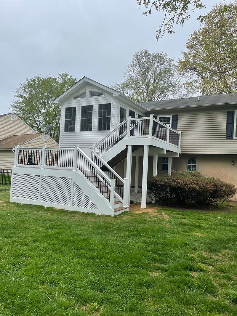 White deck and sunroom attached to a two-story house with green grass in front under an overcast sky.