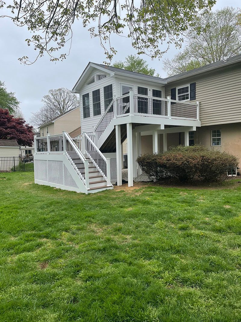 White deck with stairs attached to a house, on green grass. Overcast sky.