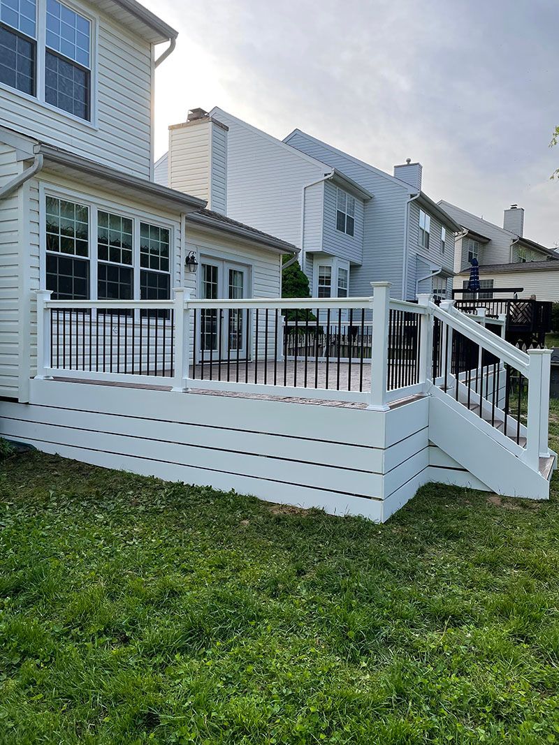 White deck with black railings, attached to a two-story house, in a backyard with green grass.