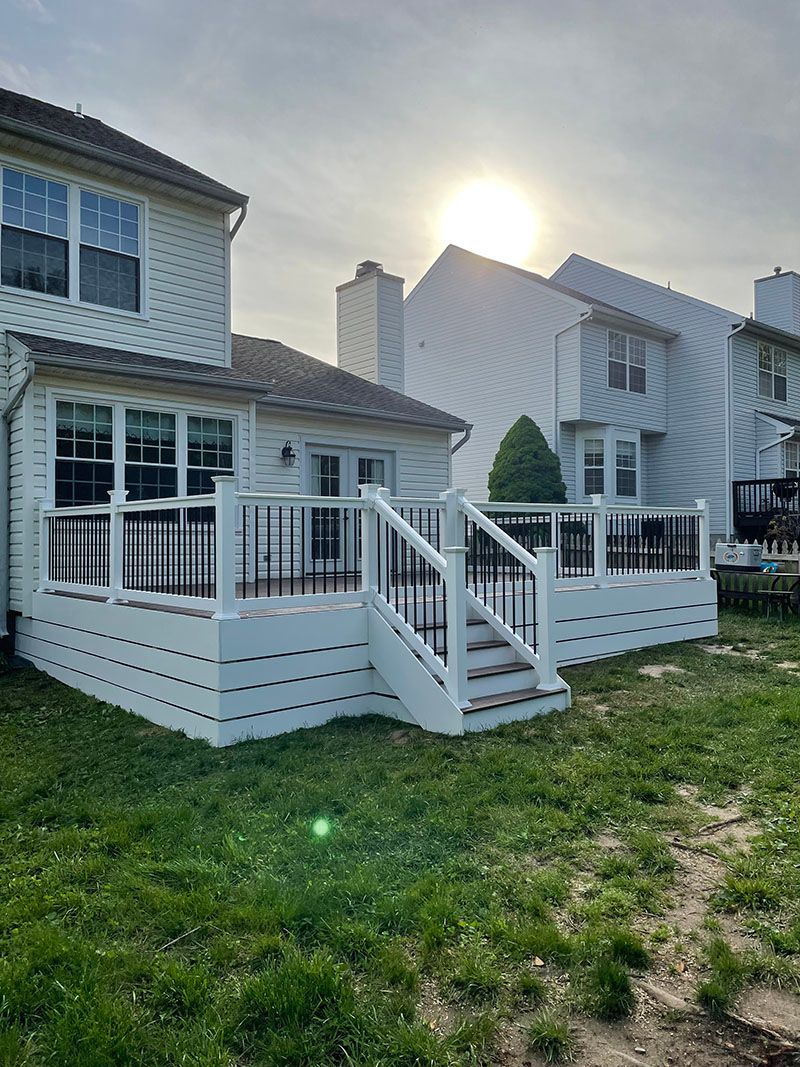 White deck with black railings attached to a house, set against a sunny sky and green grass.