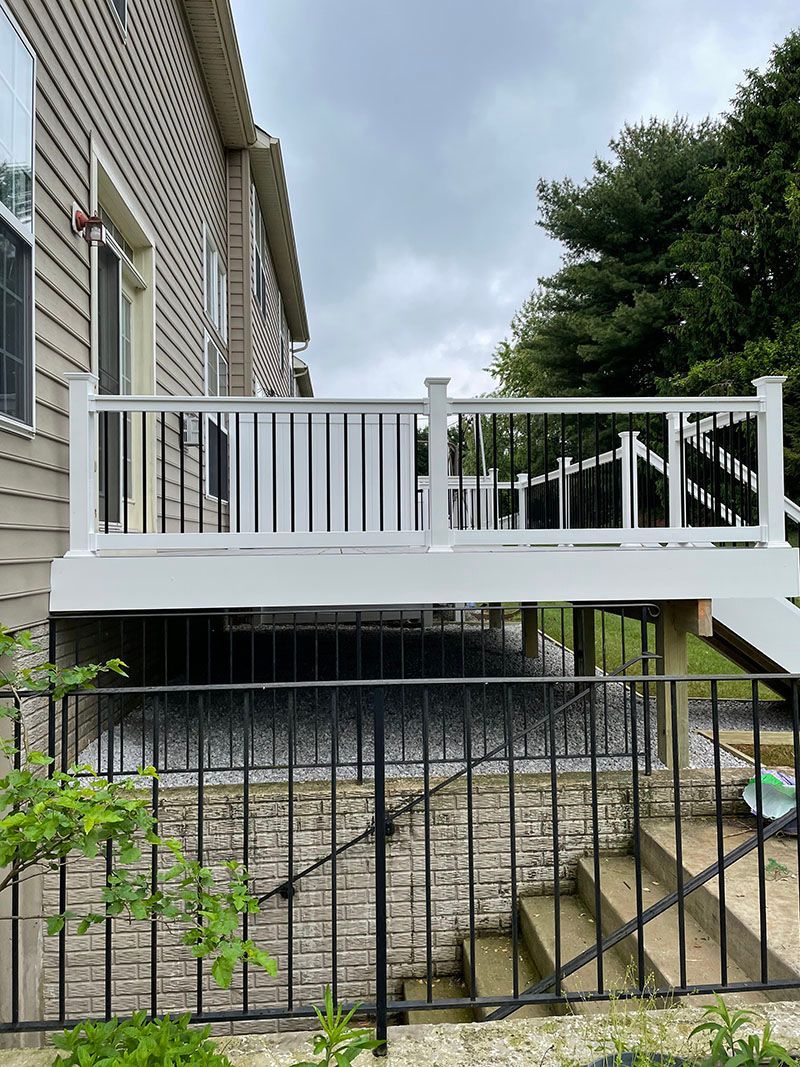 White deck with black railing and stairs, next to a house, on a cloudy day.