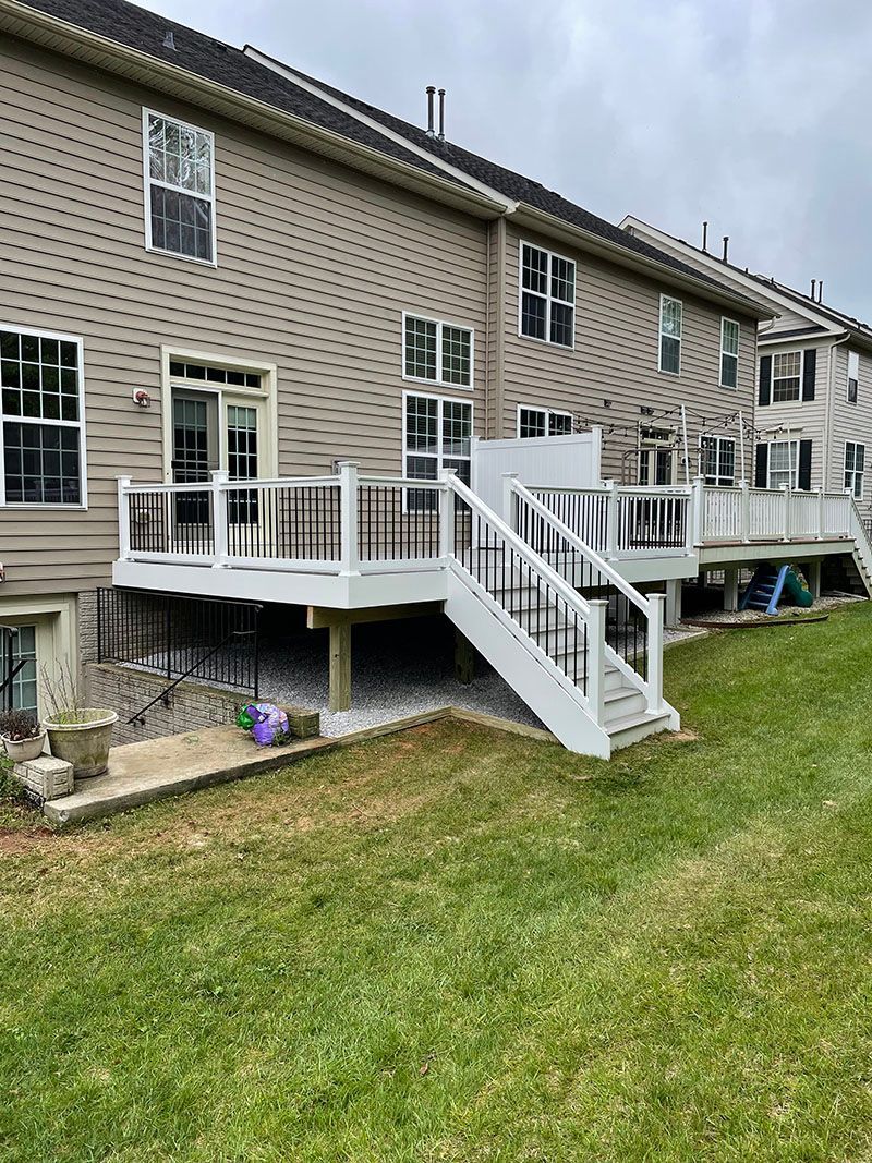Back of townhouses with multiple decks, some white, some with dark railings, on a grassy hill.