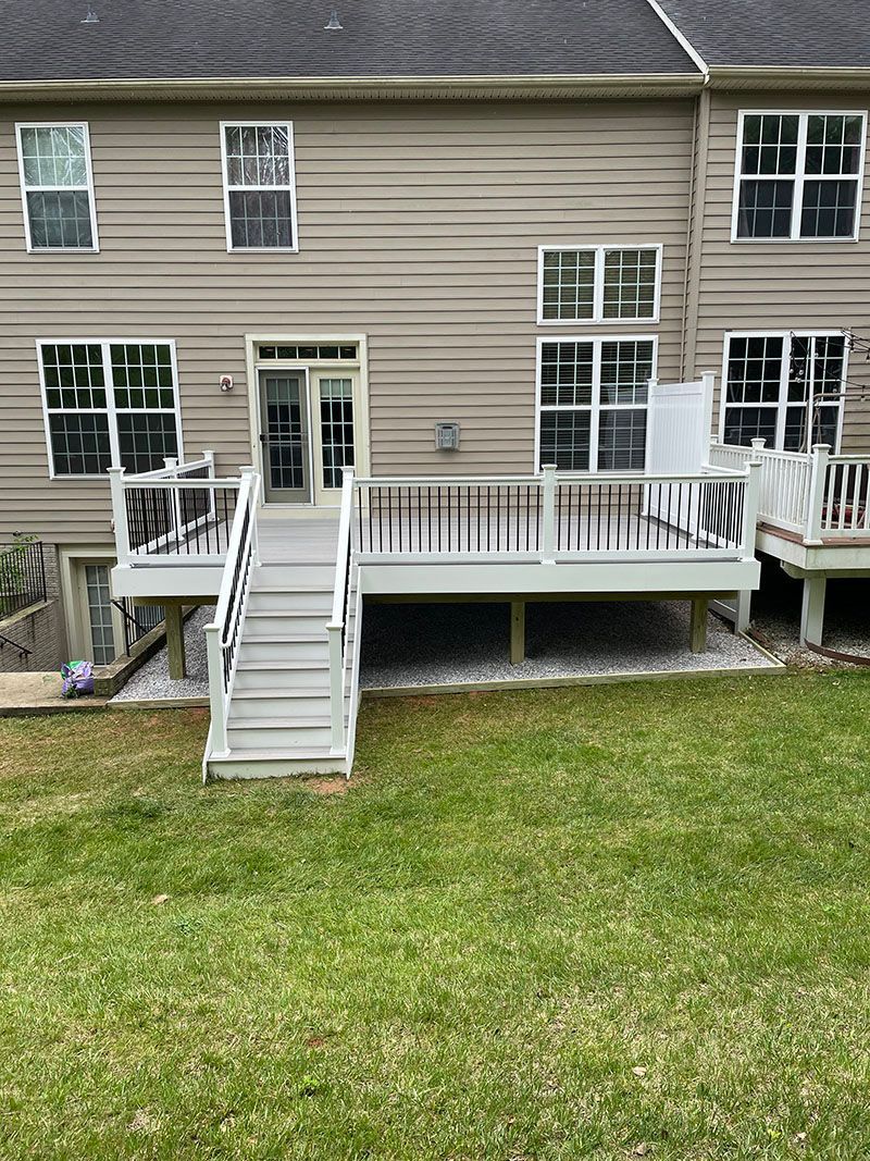 Backyard deck with stairs, light grey and white. House in background with multiple windows and a door.