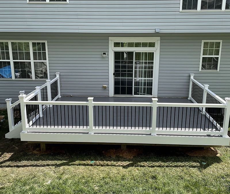 White-railed deck with black spindles in front of a light gray house with sliding glass door.