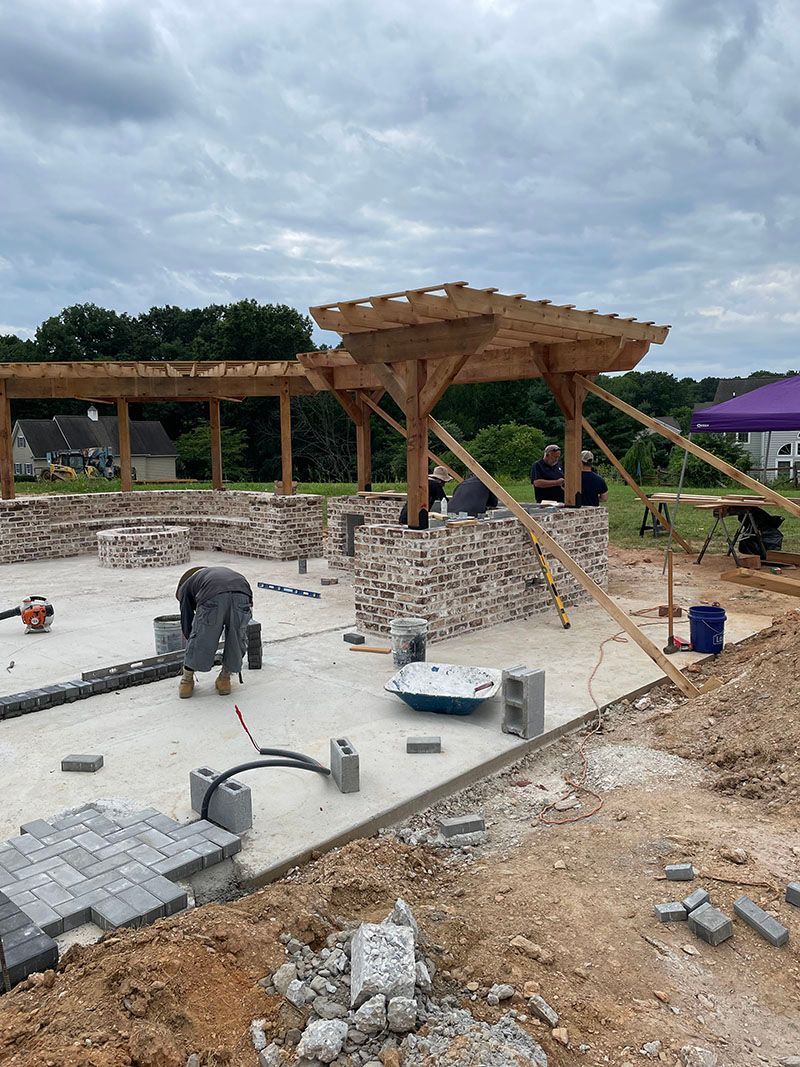 Construction site: workers installing paving stones, wooden pergola under construction.