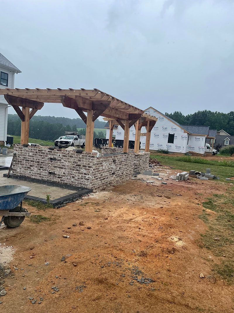 Construction site with a brick wall structure and wooden pergola. Cloudy sky, brown soil.