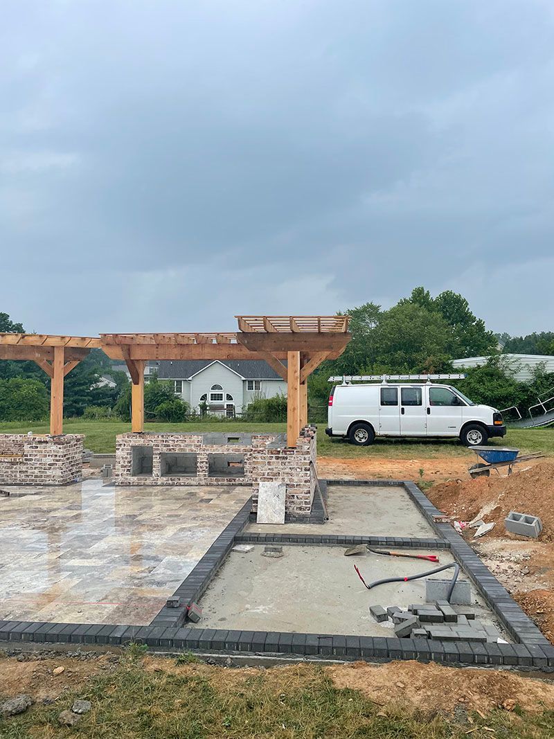 Construction site with a partially built outdoor kitchen and pergola; a white van is parked nearby.