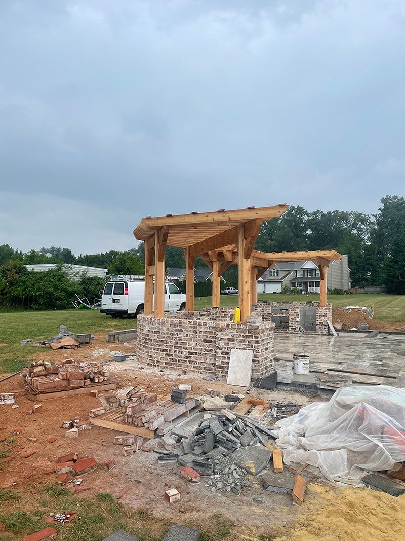 Construction site with a brick structure and wooden pergola. A white van is in the background.