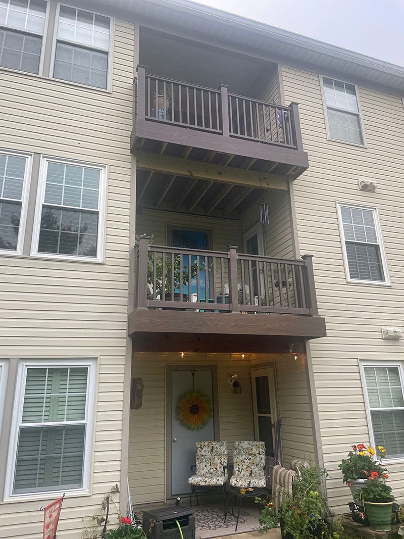 Two-story tan building with brown balconies, a yellow wreath on the door, and plants.