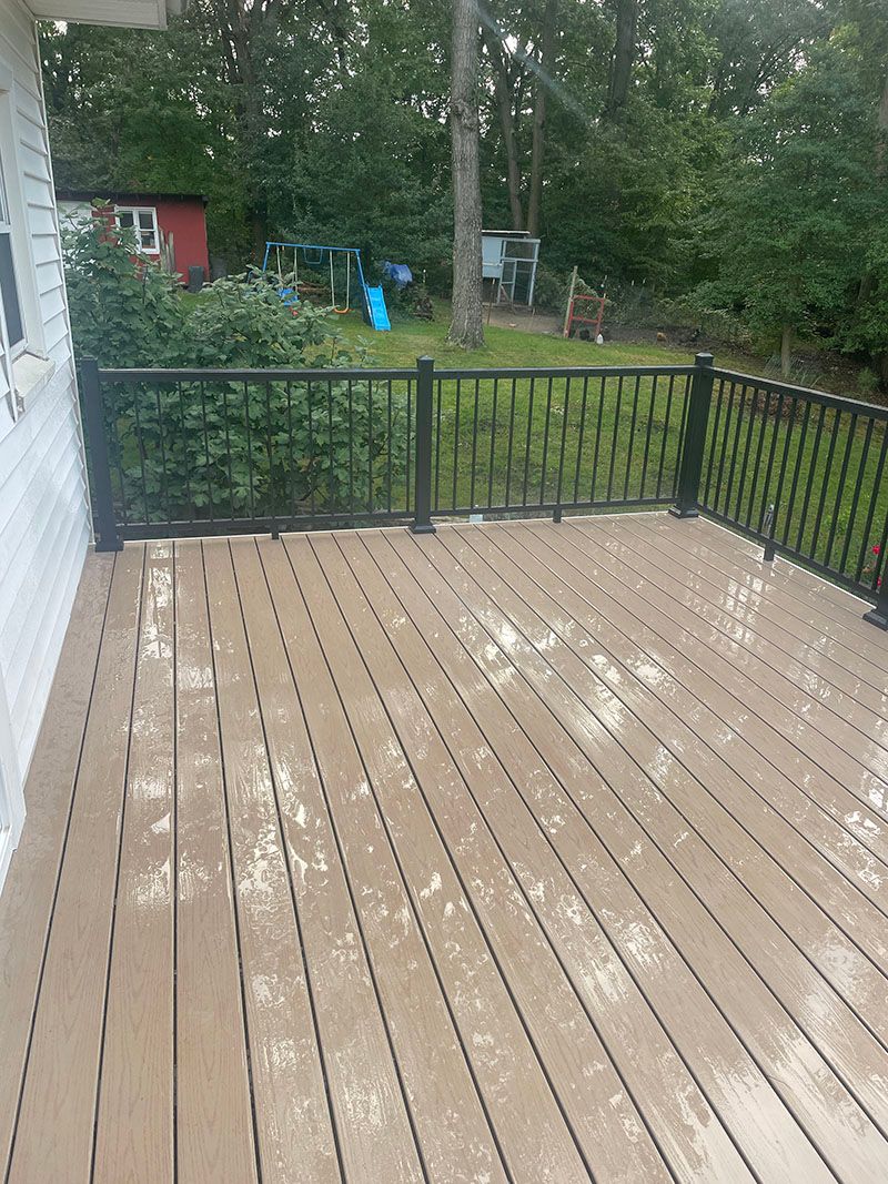 Wooden deck with black railing in a backyard setting, wet from rain.