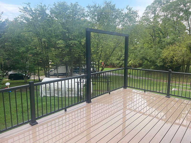 Deck with black railing and frame. Trees and a grassy area in the background. Cloudy sky.