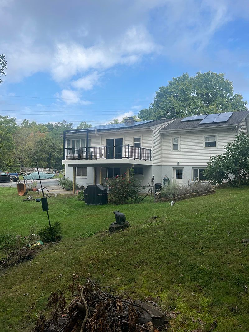 Two-story house with solar panels on the roof and a deck, viewed from a grassy yard under a cloudy sky.