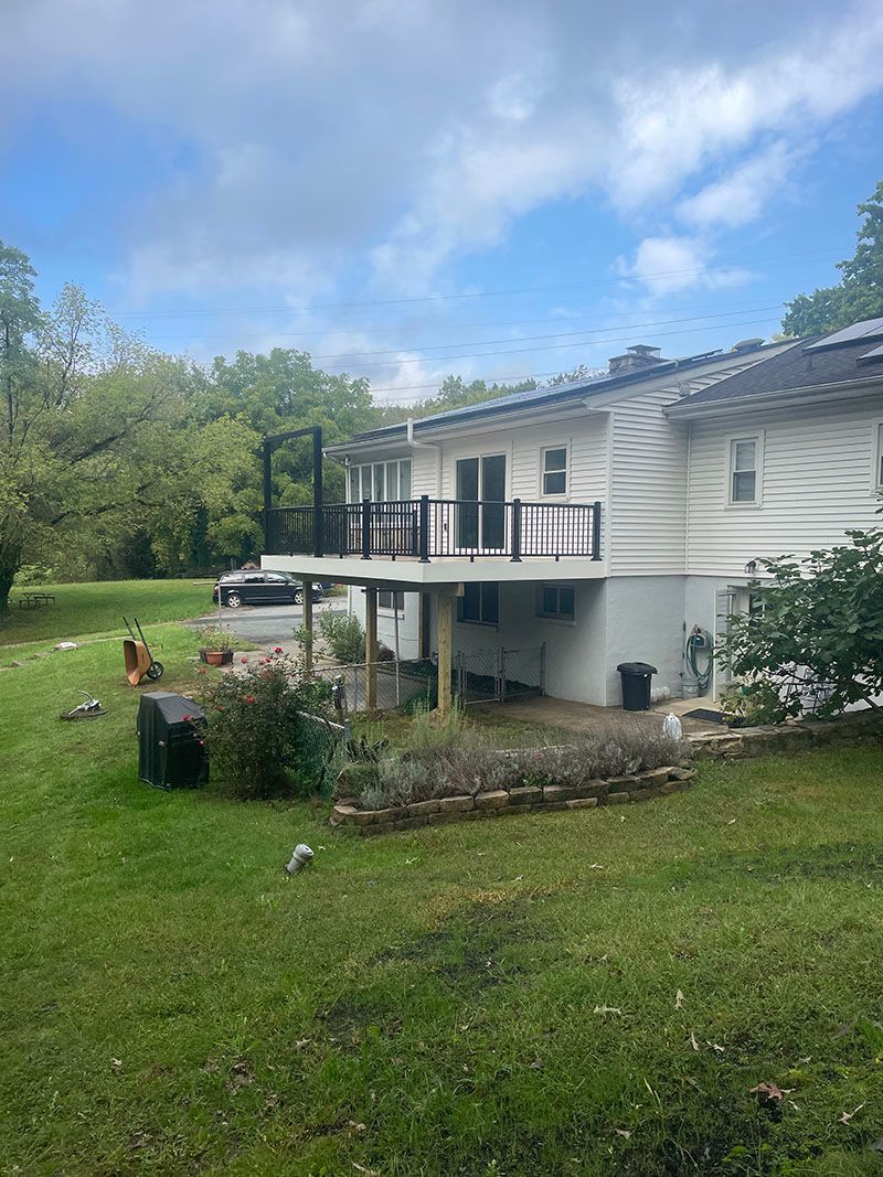 Back view of white house with a large deck, overlooking a green yard and trees.