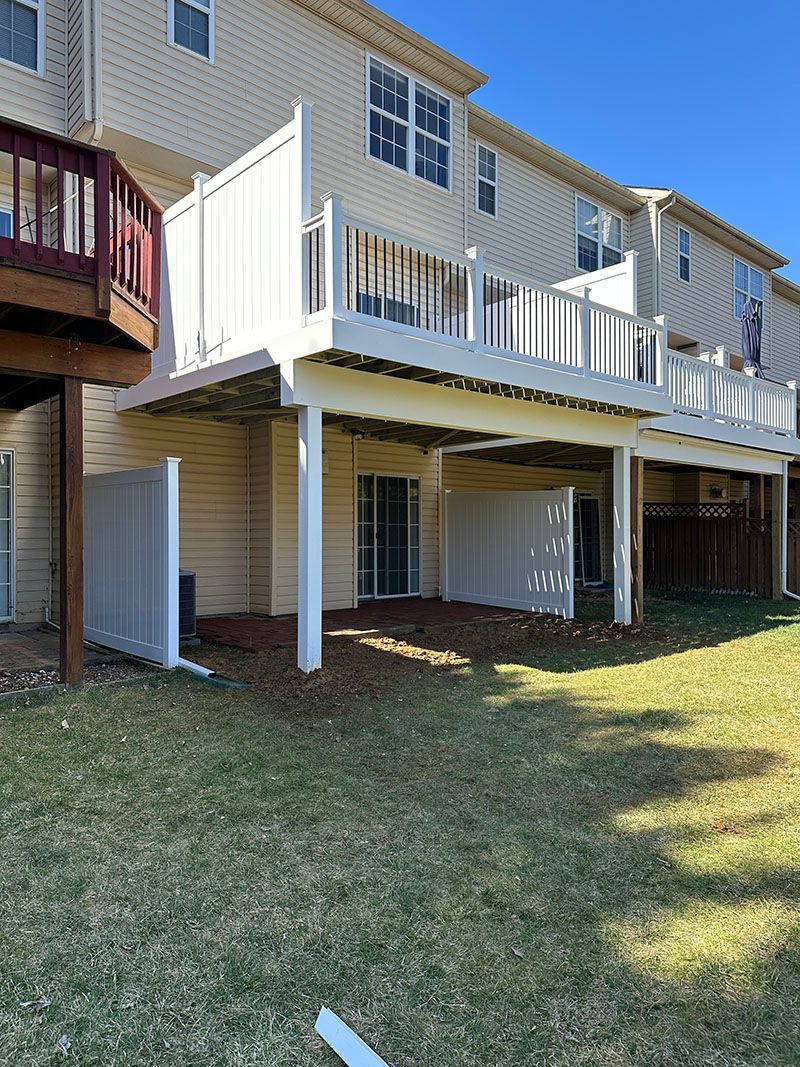 Back of a townhome with a white deck over a lower level. Cream siding and grass.