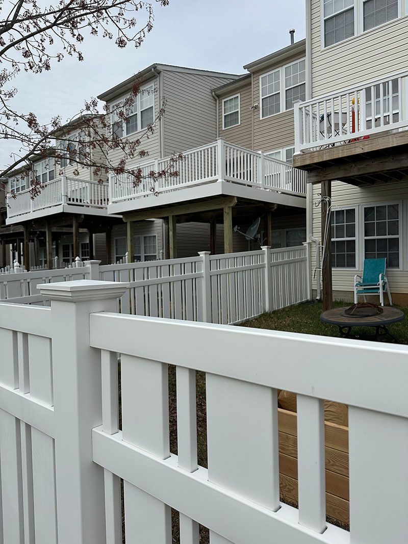 White picket fence in front of townhomes with elevated decks, overcast sky.