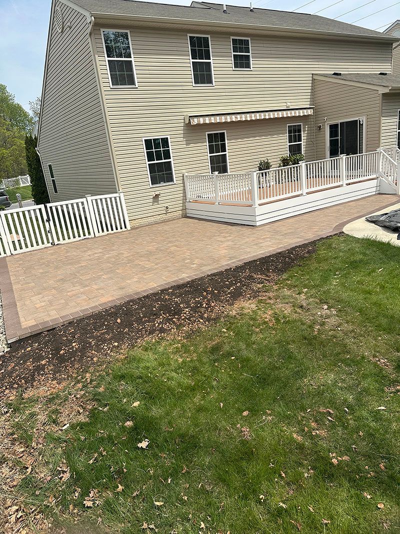Backyard with beige patio, white deck, beige house, and green lawn.