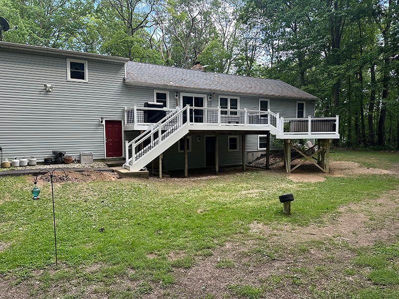 Backyard view of a two-story house with a large deck, green lawn, and surrounding trees.