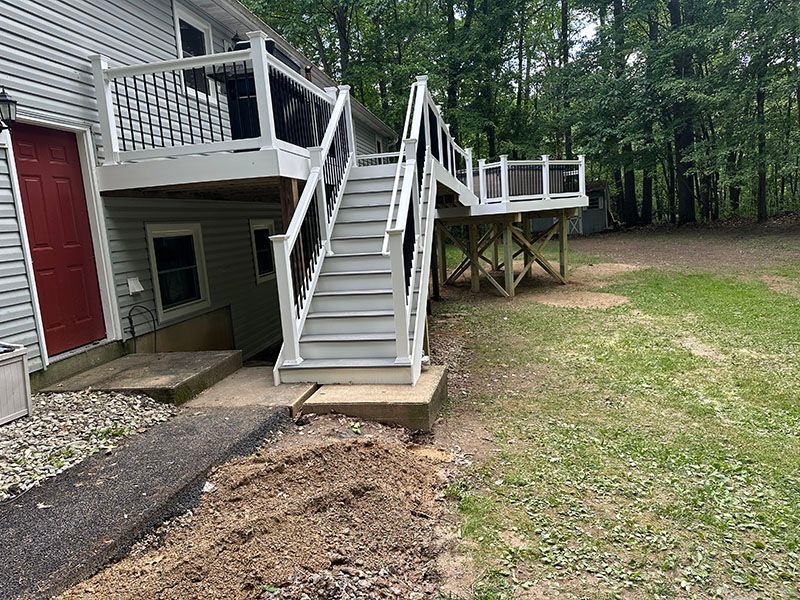 Multi-level wooden deck and stairs attached to a house; gray and white, with a grassy yard.