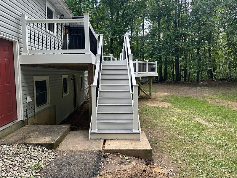 Two-story deck with stairs and a red door, gray siding, and a wooded backyard.