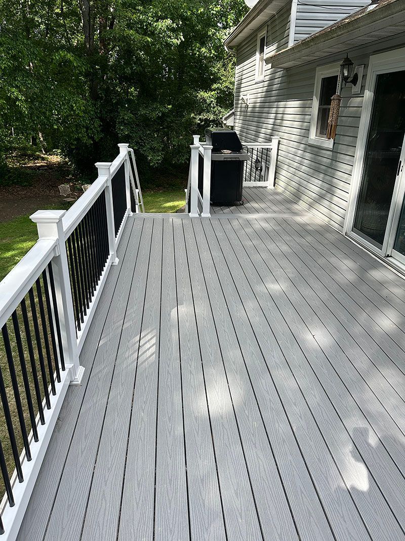 Gray deck with white railing, black balusters, and a grill next to the house.