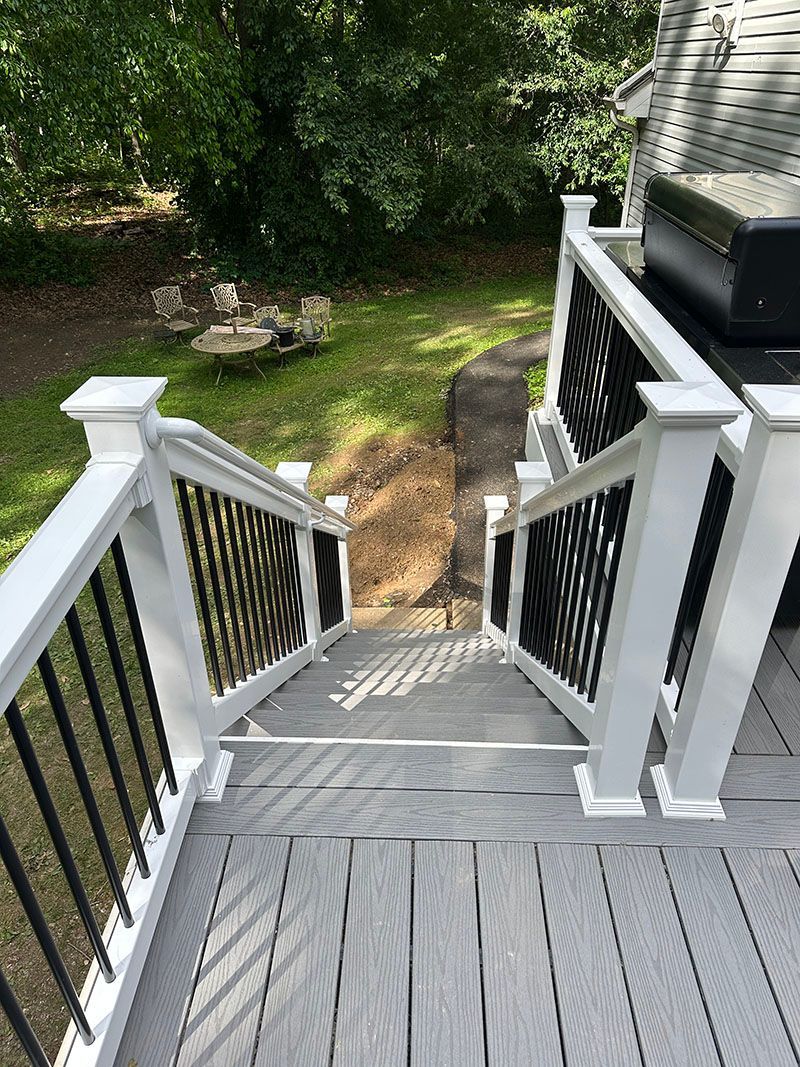 Gray deck and stairs with white railings and black balusters leading to a grassy backyard.