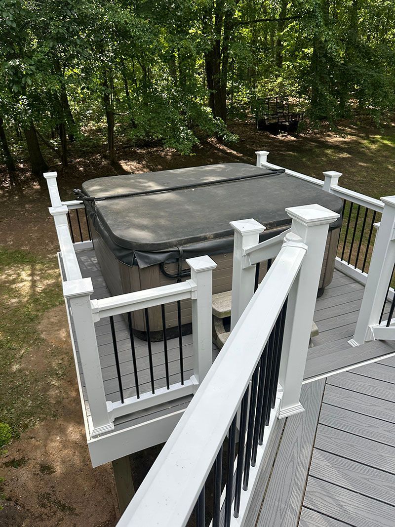 Hot tub on a deck with white railings and black spindles, surrounded by trees.
