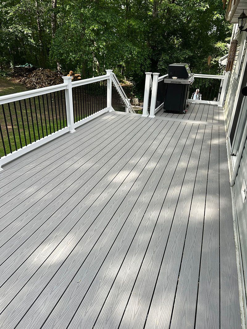 Gray composite deck with white railings and black balusters, slightly warped in the middle, with a grill in the background.