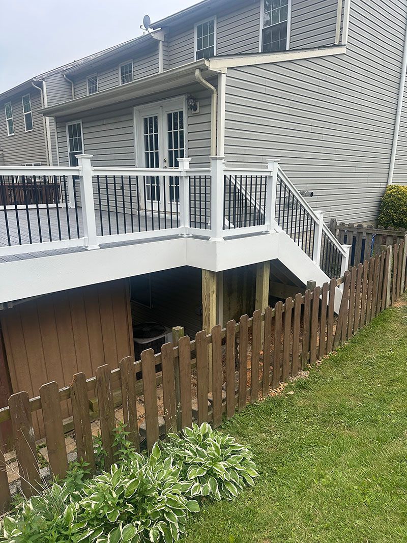 Wooden deck attached to a multi-story house, with a brown picket fence in the foreground.