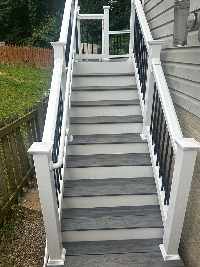 Outdoor staircase with grey steps and white and black railing.