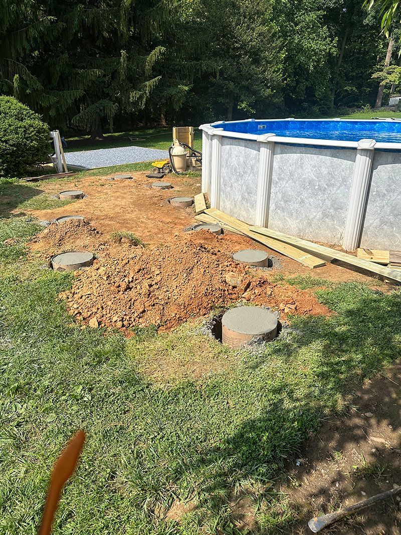 Backyard with an above-ground pool; construction site with cement pillars and disturbed earth. Green grass.