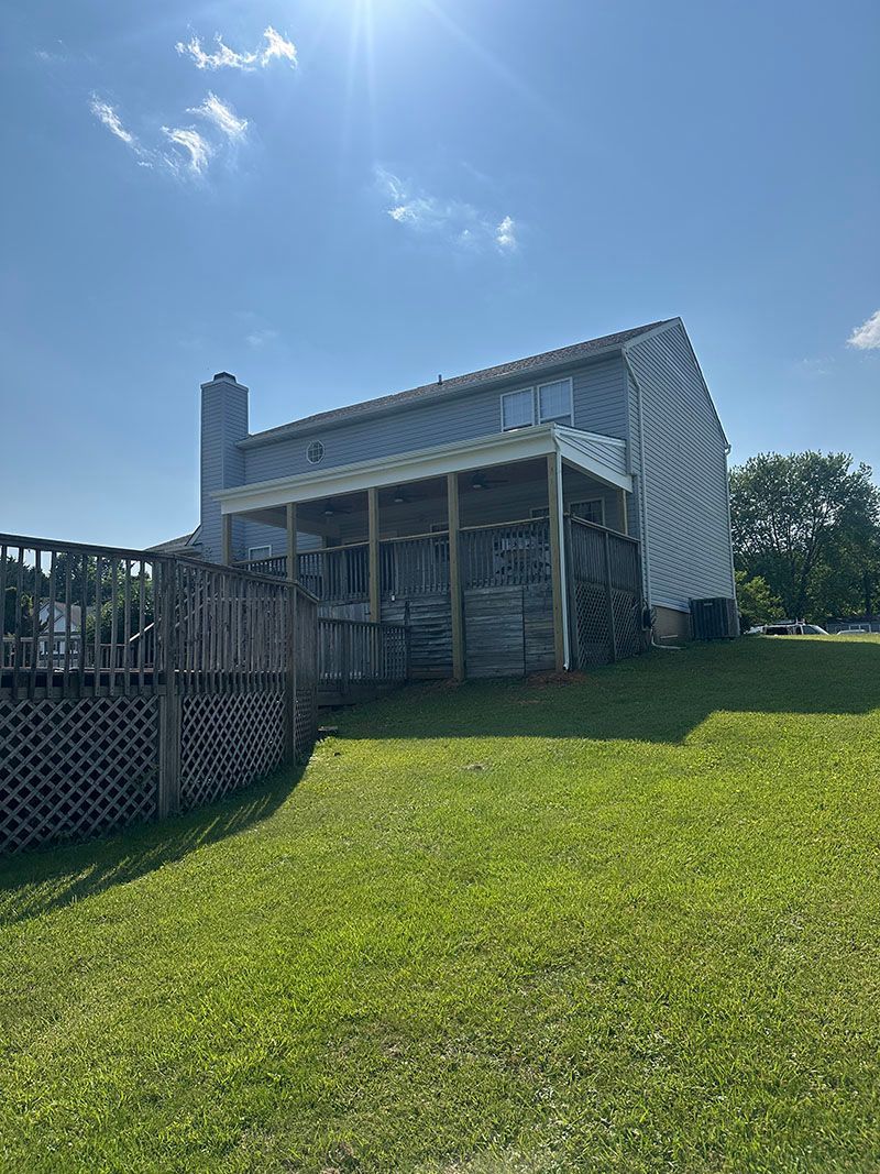 Backyard view of a house with a deck, chimney, and green lawn under a bright blue sky.