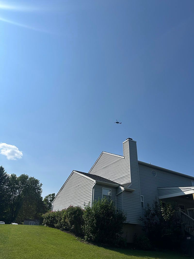 A house with a gray roof and a chimney under a blue sky with a small plane.