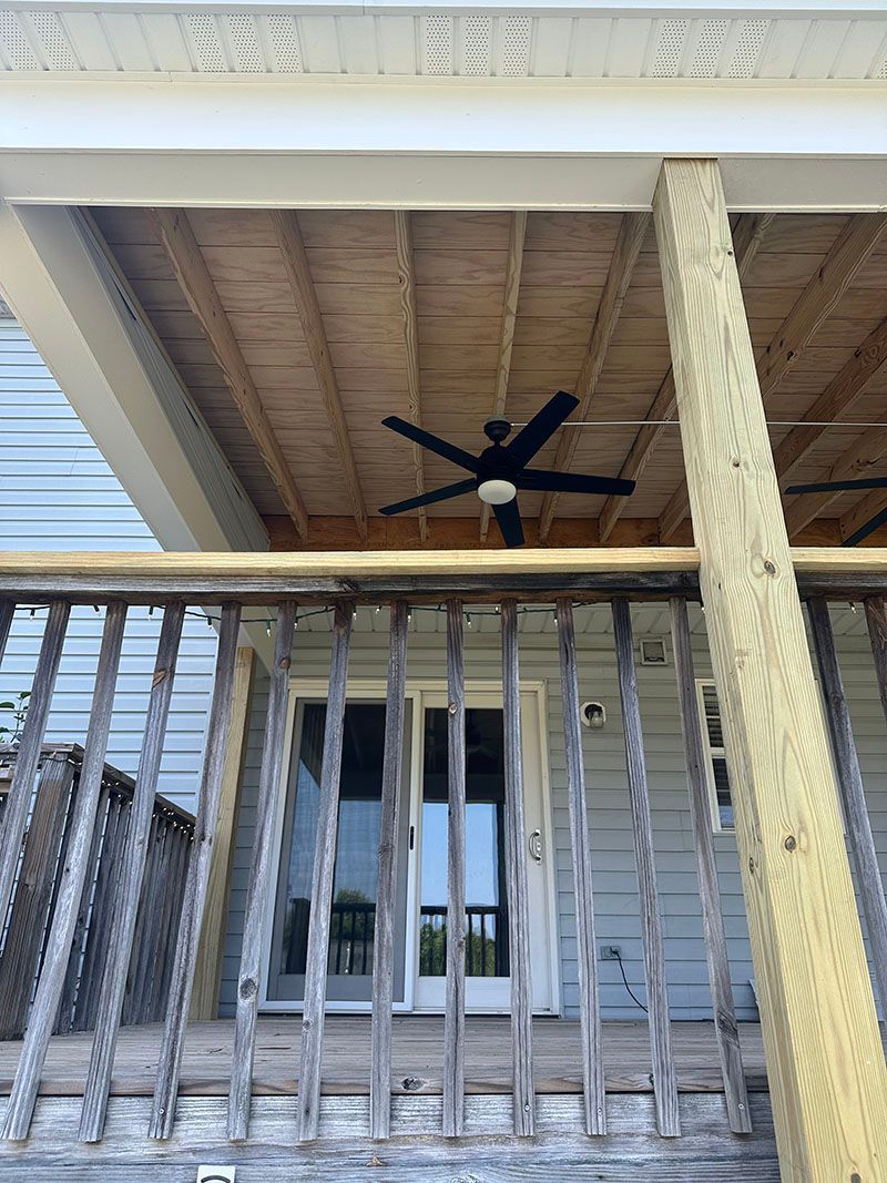 Wooden porch with a black ceiling fan, railing, and a door.