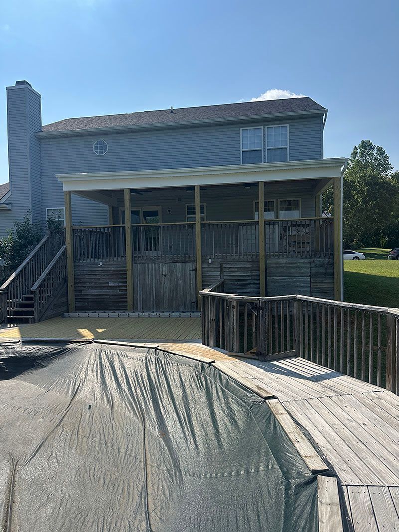 Backyard deck with roof extension; weathered wood, blue siding, sunny day.