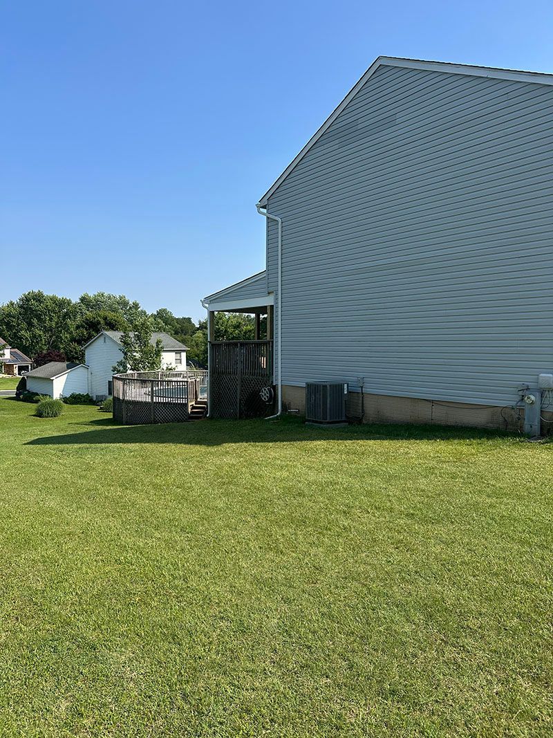 Backyard view: house with light blue siding, deck, and green lawn under a clear blue sky.