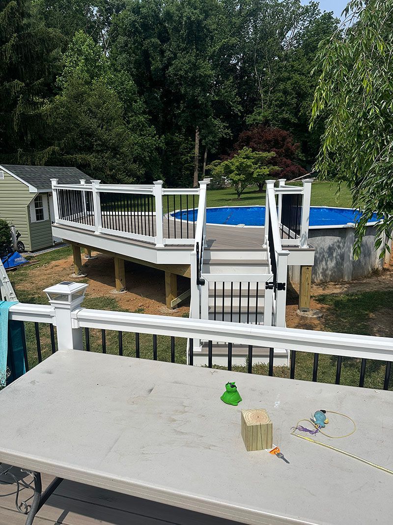 Deck with white railing and stairs leading to an above-ground pool in a backyard setting.