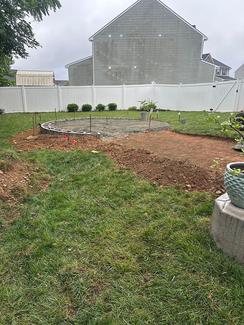 Backyard with grass, a mulched area, white fence, and a large house on a cloudy day.