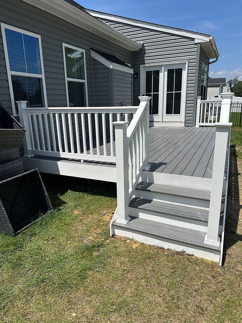Gray and white deck with steps leading to a backyard, next to a house with glass doors.