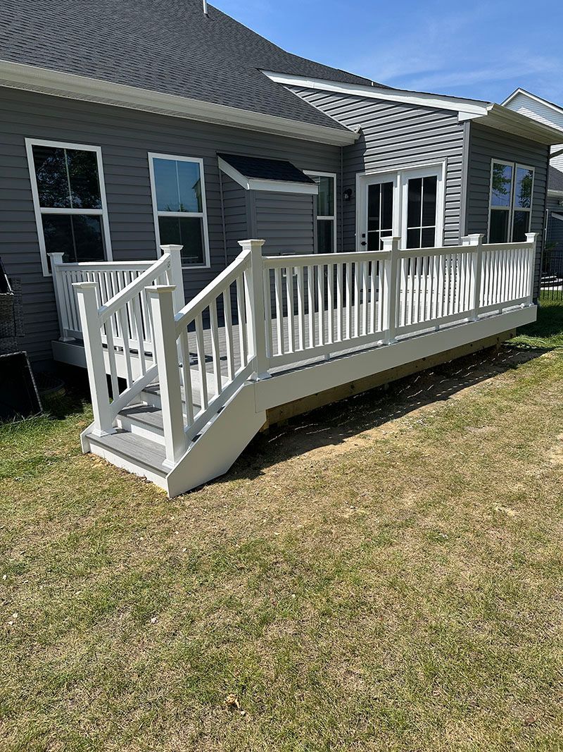 Gray house with a white deck, steps leading to a grassy backyard.