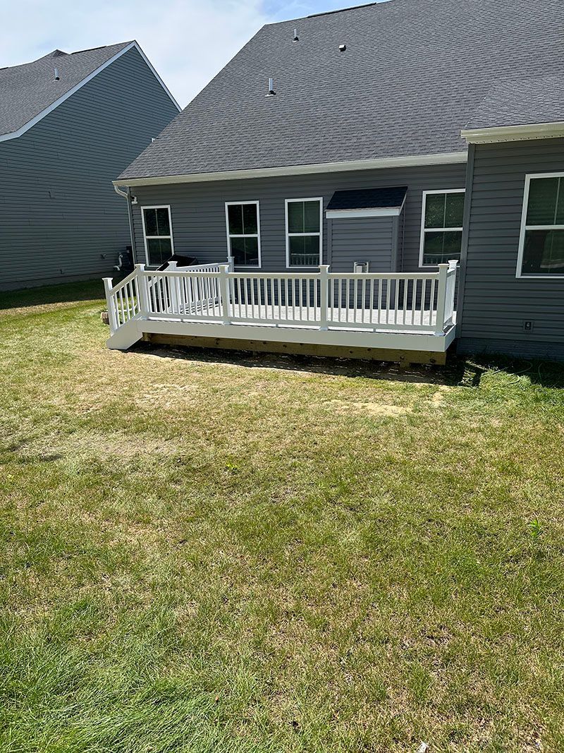 White deck on a gray house, set on brown and green grass.