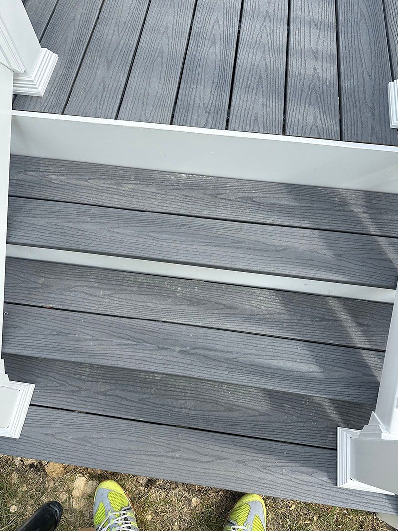 Grey deck with white trim and steps, viewed from above. Yellow shoes visible in lower frame.