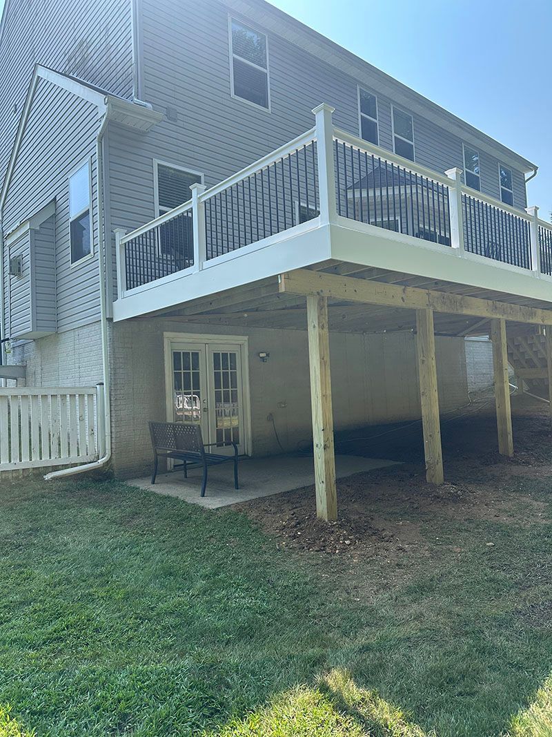 A two-story house with a large wooden deck and a door leading to a patio below.