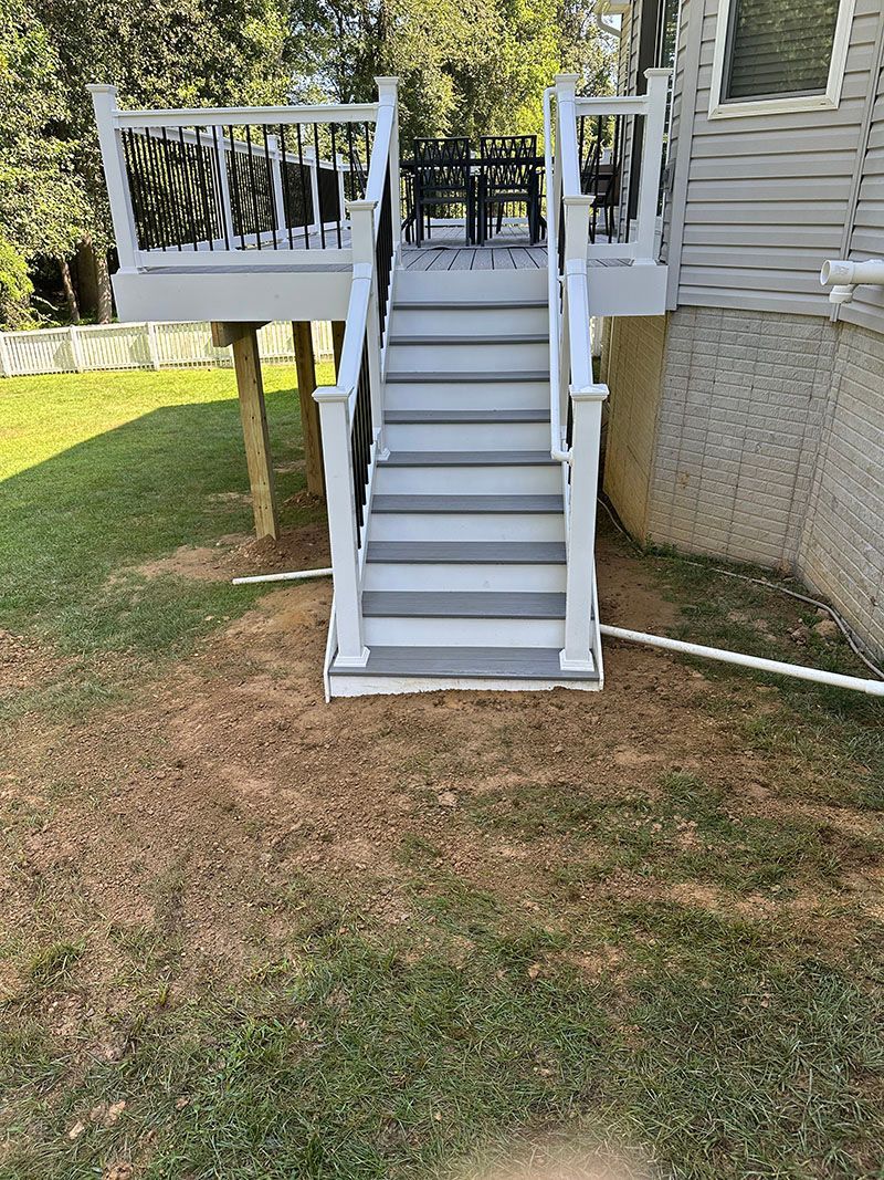 Gray stairs lead to a white deck, set against a backdrop of green grass and trees.