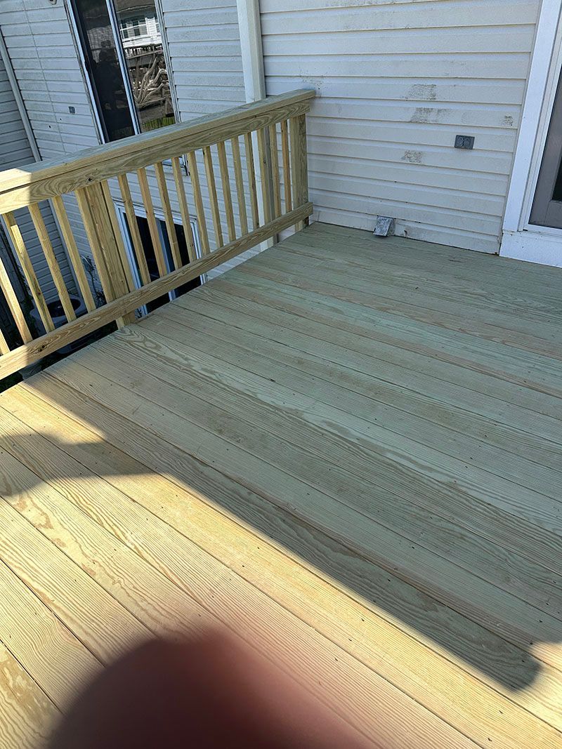 Wooden deck with railing next to a white house.
