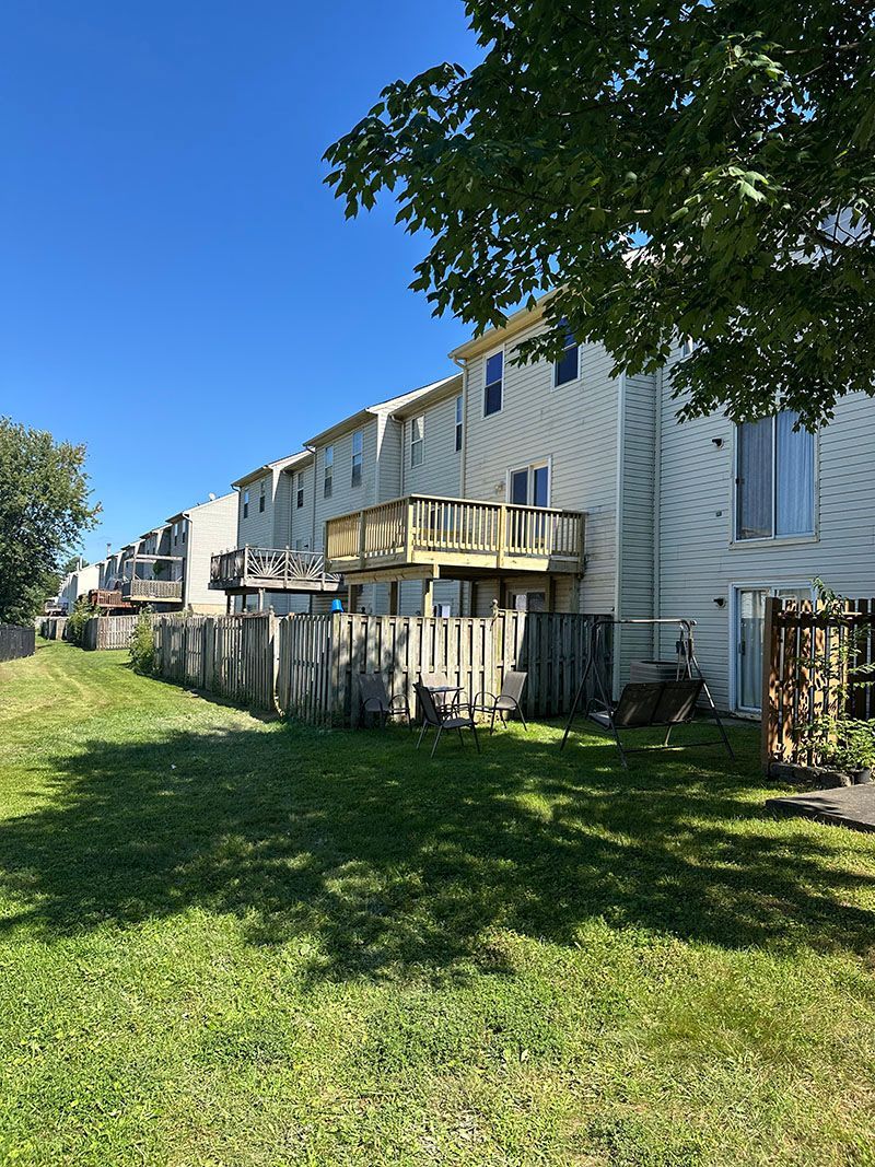 Row of townhouses with wooden decks and fences, viewed from grassy backyard on a sunny day.
