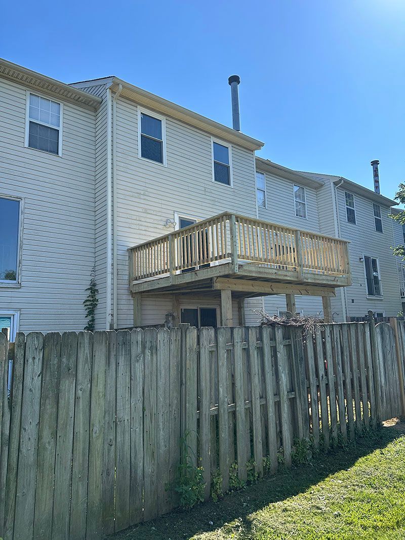 Back of a multi-story townhouse with a wooden deck, set behind a wooden fence on a sunny day.