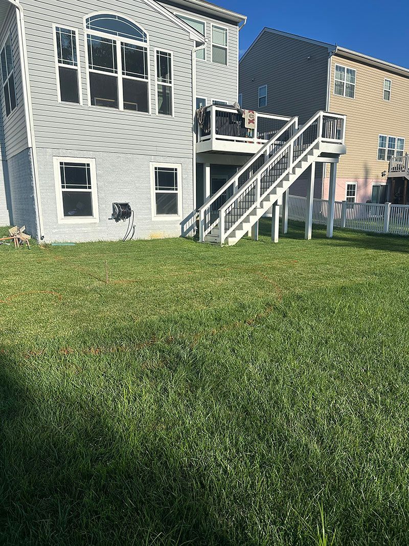 Backyard with a two-story house, wooden deck, stairs, and green grass.