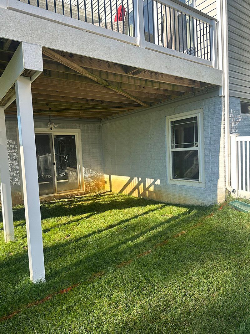 Back of house with a deck above a concrete and grass area, with a door and window.